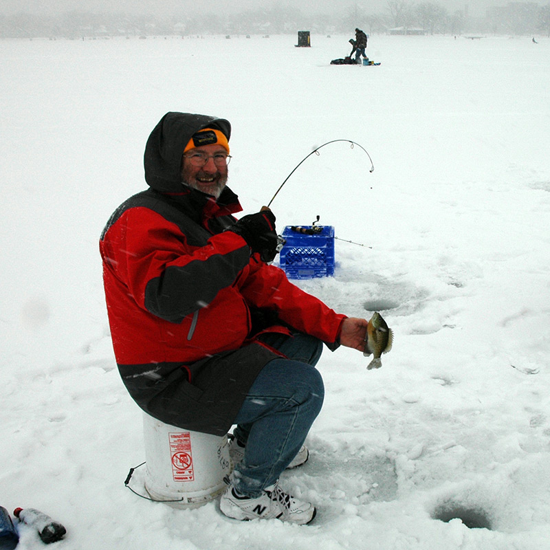 a person sits on a stool in the snow with a fishing pole