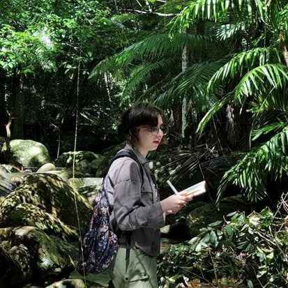 Ellie in forest doing fieldwork holding notebook and pen