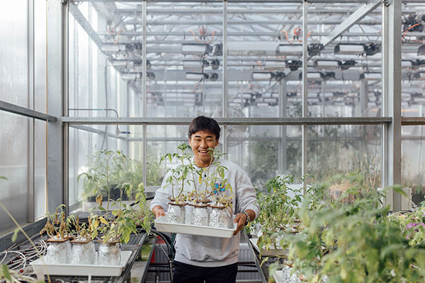 Student carrying tray of seedling through greenhouse